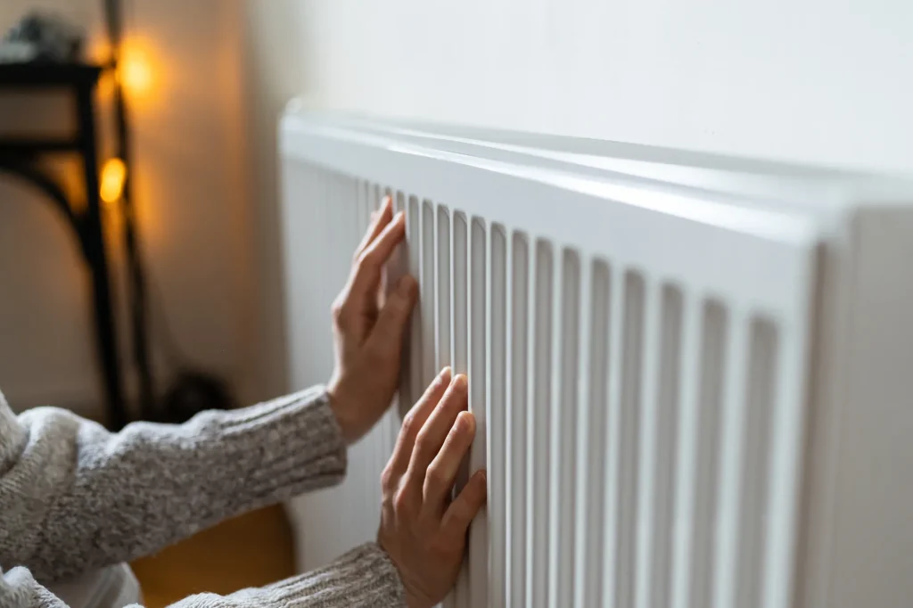 woman in sweater puts hands on room heater