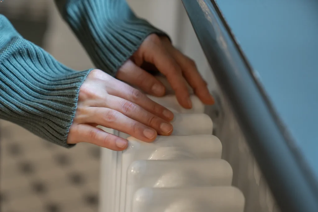 woman warming hands near old vintage radiator