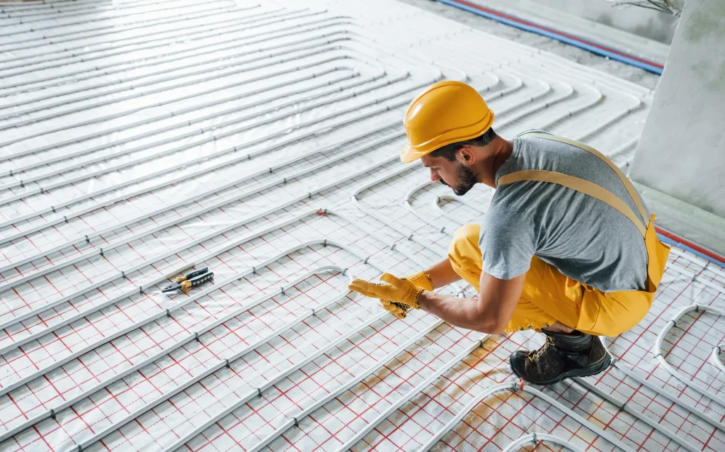 worker in yellow colored uniform installing underfloor heating in King's Lynn
